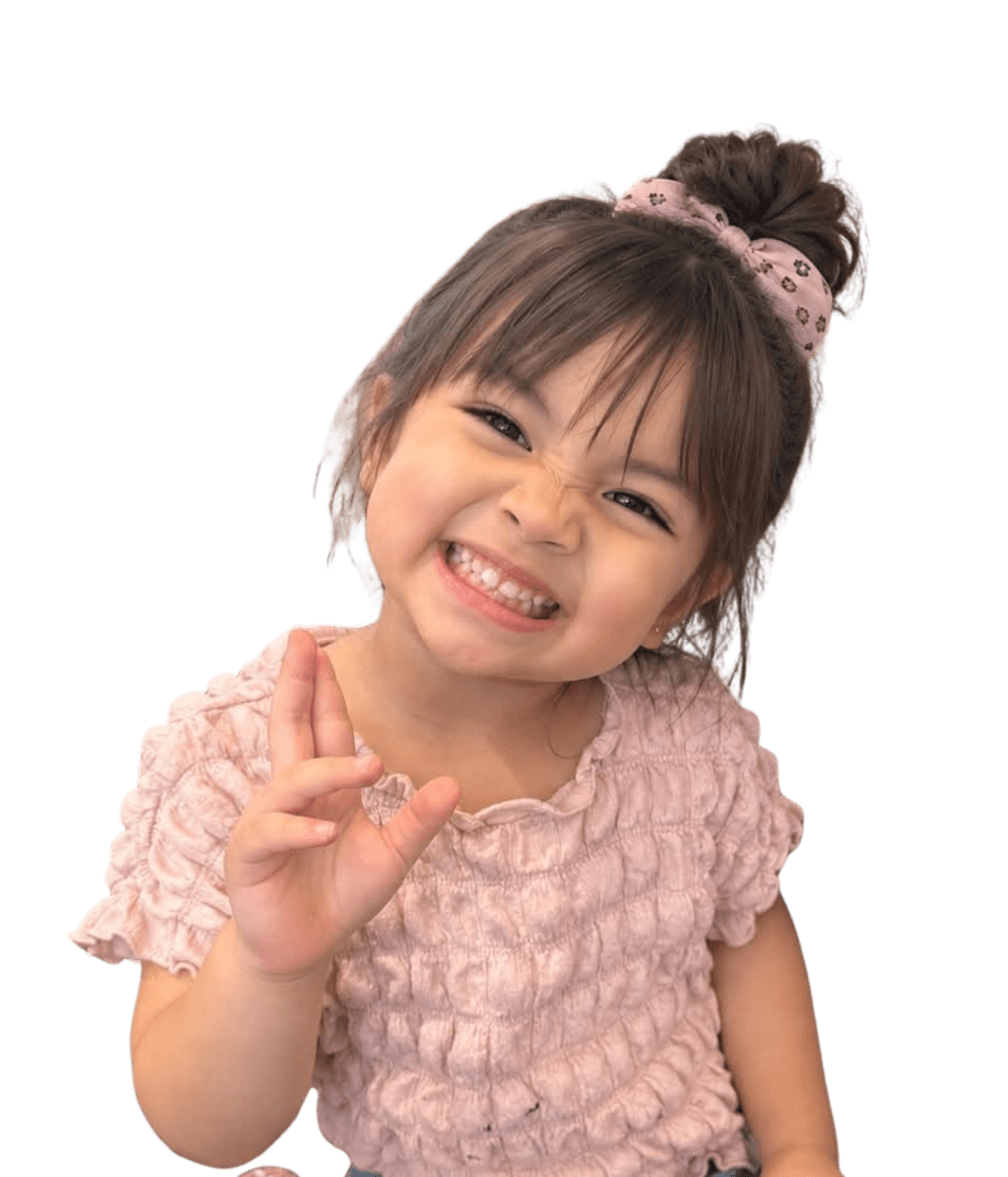Leticia Khloe, smiling and waving, wearing a pink top and a pink hair scrunchie